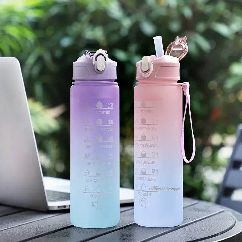 Two gradient water bottles on a table with a laptop, outdoors.